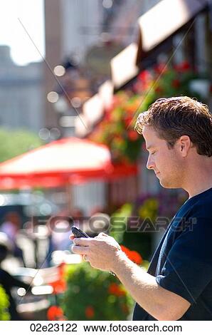 Stock Image - Man using cellular PDA in front of summer street cafe.. Fotosearch