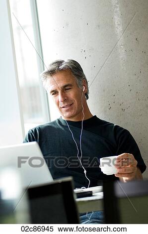 Stock Photography - Middle-aged man listening to music in urban cafe.. Fotosearch
