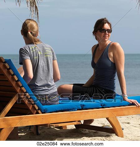 Mother and teenage daughter sitting on a sun lounger on the beach. View Large Photo Image Picture - Mother and teenage daughter sitting on a sun lounger on the beach. . Fotosearch