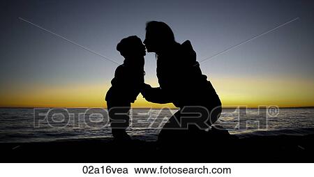 Mother kneels kissing child at waters edge, sunset View Large Photo Image Stock Image - Mother kneels kissing child at waters edge, sunset. Fotosearch