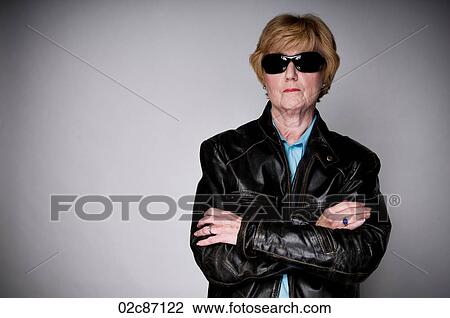Stock Image - Older senior woman in a black leather jacket and sunglasses.. Fotosearch