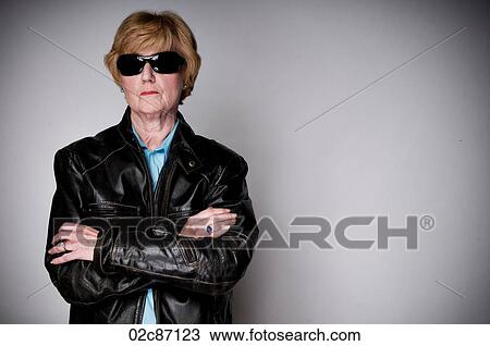 Stock Image - Older senior woman in a black leather jacket and sunglasses.. Fotosearch
