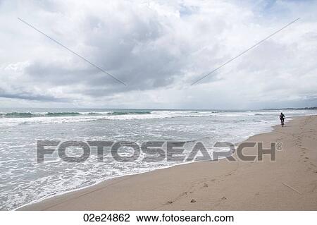 Stock Image - Person walking along beach in Bali. Fotosearch