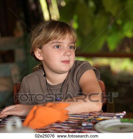 Portrait of young girl sitting at a table looking to the side. View Large Photo Image Stock Photograph - Portrait of young girl sitting at a table looking to the side. . Fotosearch