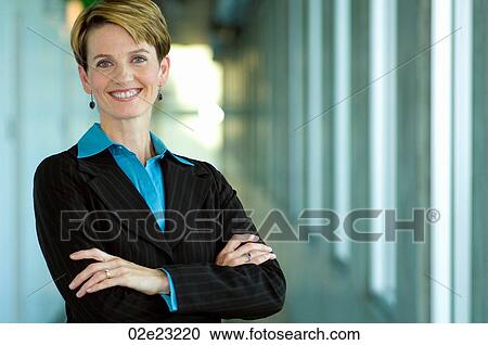 Professional female executive folding arms while standing in hallway. View Large Photo Image Stock Image - Professional female executive folding arms while standing in hallway.. Fotosearch