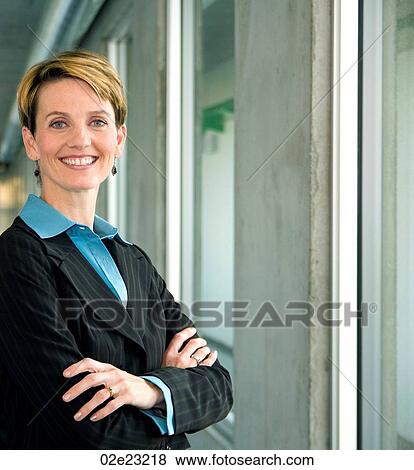 Professional female executive folding arms while standing in hallway. View Large Photo Image Stock Photo - Professional female executive folding arms while standing in hallway.. Fotosearch