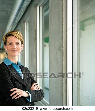 Stock Photo - Professional female executive folding arms while standing in hallway.. Fotosearch