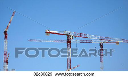 Stock Photo - Red and White construction cranes against blue sky.. Fotosearch