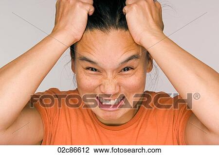 Stock Image - Stressed out Asian woman holding head with hands.. Fotosearch