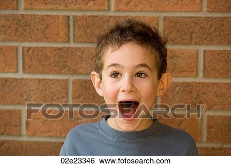 Stock Photograph - Surprised shot of young boy against brick wall.. Fotosearch