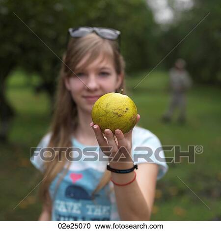 Stock Image - Teenage girl smiling holding fruit. . Fotosearch