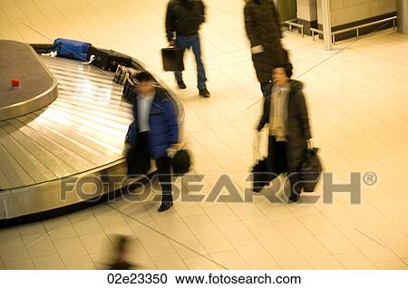Stock Image - Travelers collecting luggage from airport baggage carousel.. Fotosearch