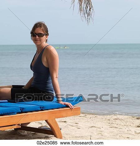 Stock Photography - Woman sitting on a sun lounger on the beach. . Fotosearch