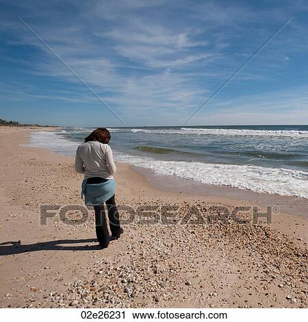 Stock Image - Woman walking along the seashore in the Hamptons. Fotosearch