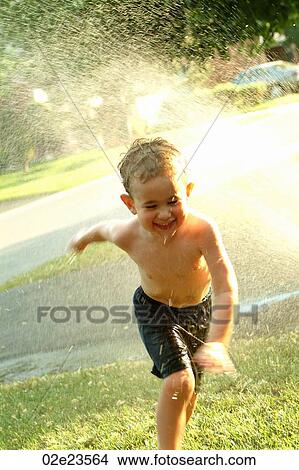 Young boy running through summer sprinkler. View Large Photo Image Picture - Young boy running through summer sprinkler.. Fotosearch