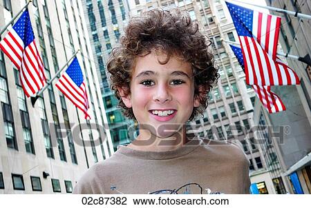 Stock Image - Young boy smiling with American flags and buildings in background.. Fotosearch
