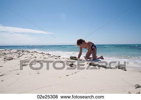 Stock Photo - Young girl digging in sand on beach at Belizean Isle in Belize. Fotosearch