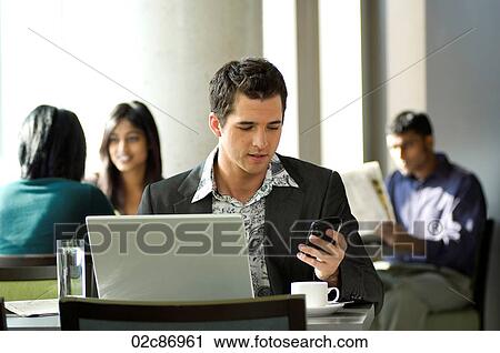 Stock Image - Young urban businessman using Blackberry PDA and wireless laptop in a hotspot cafe.. Fotosearch