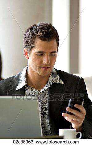 Stock Image - Young urban businessman using Blackberry PDA and wireless laptop in a hotspot cafe.. Fotosearch