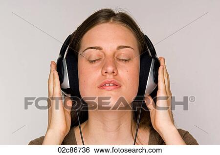 Stock Photograph - Young woman intently listening to music on headphones.. Fotosearch