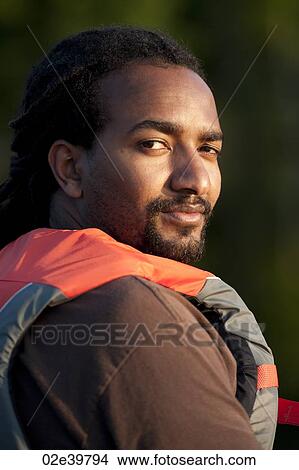 Africian American wearing a life jacket looking over his shoulder at the camera View Large Photo Image Picture - Africian American wearing a life jacket looking over his shoulder at the camera. Fotosearch