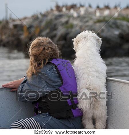 Stock Photo - Back view of young girl with her dog in a boat at Lake of the Woods, Ontario. Fotosearch
