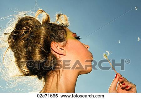 Stock Photography - Close-up of an attractive women blowing a dandelion. Fotosearch