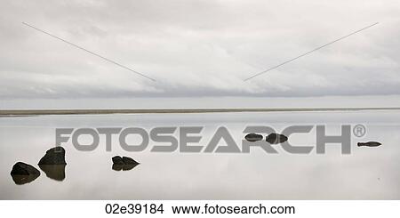 Cloudy sky, reflected in calm water, with rocks breaking the ocean surface View Large Photo Image Picture - Cloudy sky, reflected in calm water, with rocks breaking the ocean surface. Fotosearch