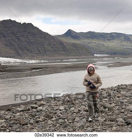 Stock Image - Eroding mountain next to glacial riverbank and rocky moraine with girl. Fotosearch
