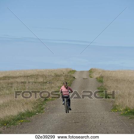 Stock Photo - Girl riding bicycle on empty rural road. Fotosearch