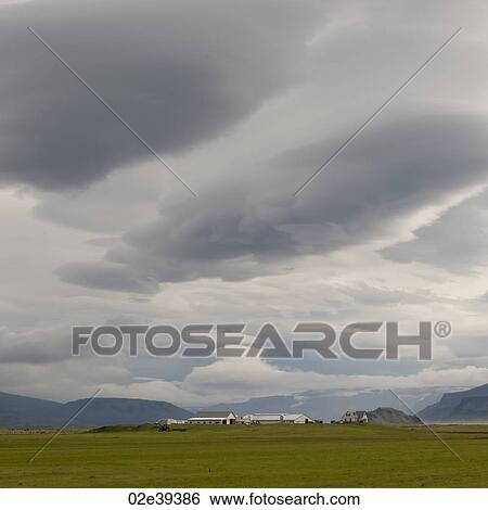 Stock Photograph - Landscape, cloudy sky over farmyard and distant mountain. Fotosearch