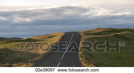 Stock Photo - Landscape, highway disappearing over the horizon through farmland, on a cloudy day. Fotosearch