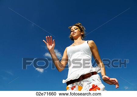 Stock Image - Low angle photograph of a woman in a white top against a blue sky. Fotosearch