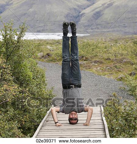 Man doing headstand on boardwalk in hilly countryside View Large Photo Image Stock Image - Man doing headstand on boardwalk in hilly countryside. Fotosearch