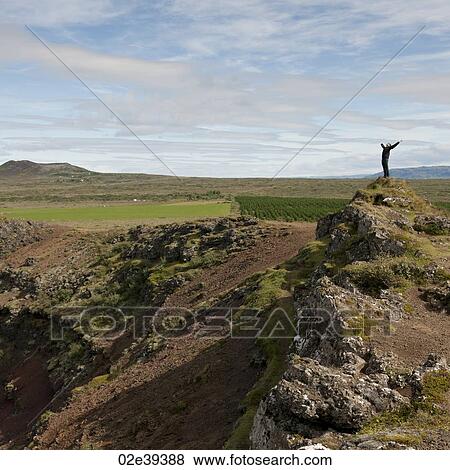 Man stretching with open arms on rocky hill outcrop above agricultural lands View Large Photo Image Stock Photo - Man stretching with open arms on rocky hill outcrop above agricultural lands. Fotosearch