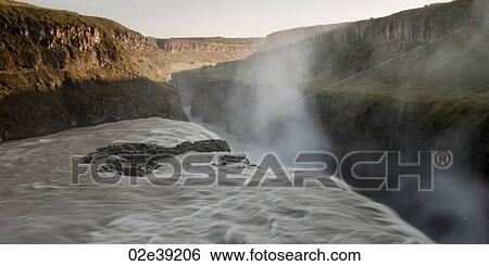 Stock Photograph - Misty waterfall off cliff into canyon. Fotosearch