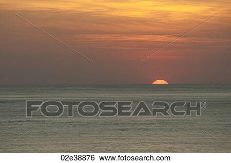 Stock Photograph - Orange clouded sunset over the calm ocean horizon. Fotosearch