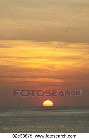 Stock Photography - Orange clouded sunset over the calm ocean horizon. Fotosearch