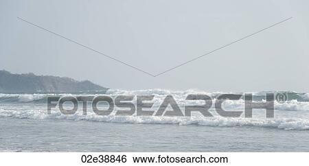 Overcast day at the seaside with waves lapping up against the sandy beach View Large Photo Image Stock Photograph - Overcast day at the seaside with waves lapping up against the sandy beach. Fotosearch