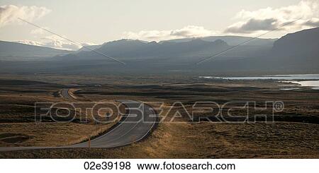 Paved highway meandering through dry farmland towards misty mountains View Large Photo Image Stock Photo - Paved highway meandering through dry farmland towards misty mountains. Fotosearch