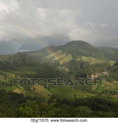 Stock Image - Rainbow over a field, Thailand. Fotosearch