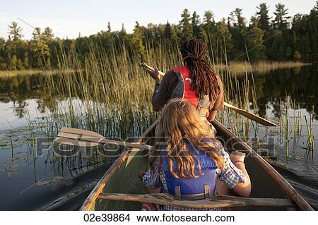 Rear view of blond girl and Africian American man rowing in a canoe at Lake of the Woods, Ontario View Large Photo Image Picture - Rear view of blond girl and Africian American man rowing in a canoe at Lake of the Woods, Ontario. Fotosearch