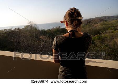 Rear view of woman looking over the hill tops at the horizon from a balcony View Large Photo Image Picture - Rear view of woman looking over the hill tops at the horizon from a balcony. Fotosearch