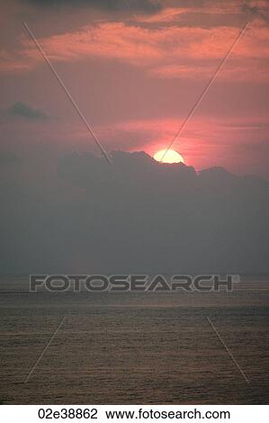 Stock Image - Red evening sunset over the ocean hidden behind the clouds. Fotosearch