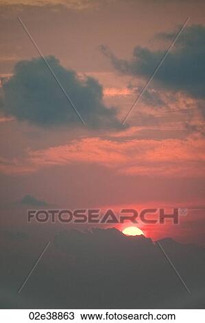 Stock Image - Red evening sunset over the ocean hidden behind the clouds. Fotosearch