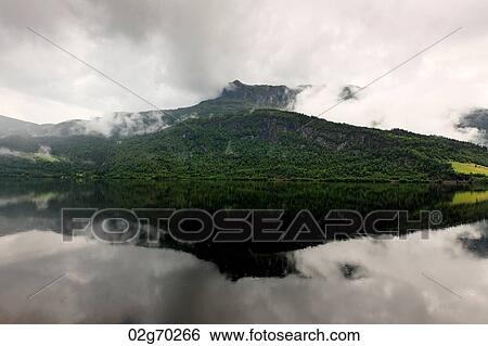 Reflection of mountain with clouds in the lake, Granvinsvatnet, Granvin, Hordaland County, Norway View Large Photo Image Stock Photograph - Reflection of mountain with clouds in the lake, Granvinsvatnet, Granvin, Hordaland County, Norway. Fotosearch