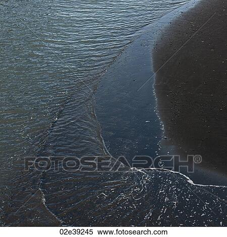 Stock Photography - Rippled waters on the volcanic sand shoreline. Fotosearch