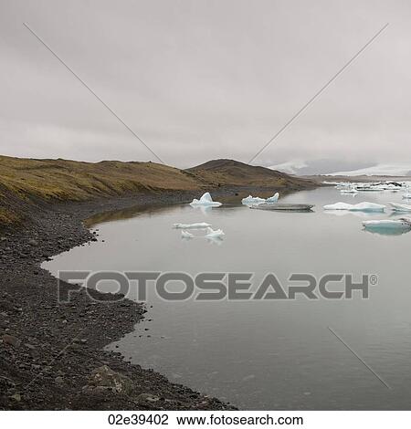 Stock Image - Rocky beach on glacial lake with floating icebergs. Fotosearch