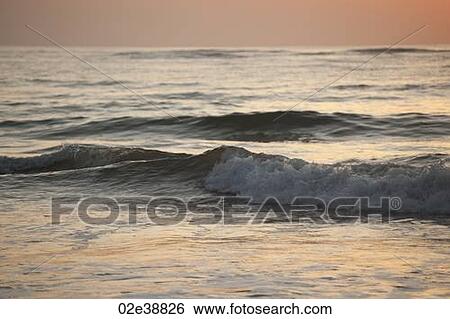 Rolling waves on the ocean in the evening glow View Large Photo Image Stock Photograph - Rolling waves on the ocean in the evening glow. Fotosearch