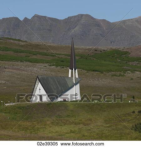 Stock Photography - Rural Christian church hidden behind pastureland hillside before mountain. Fotosearch